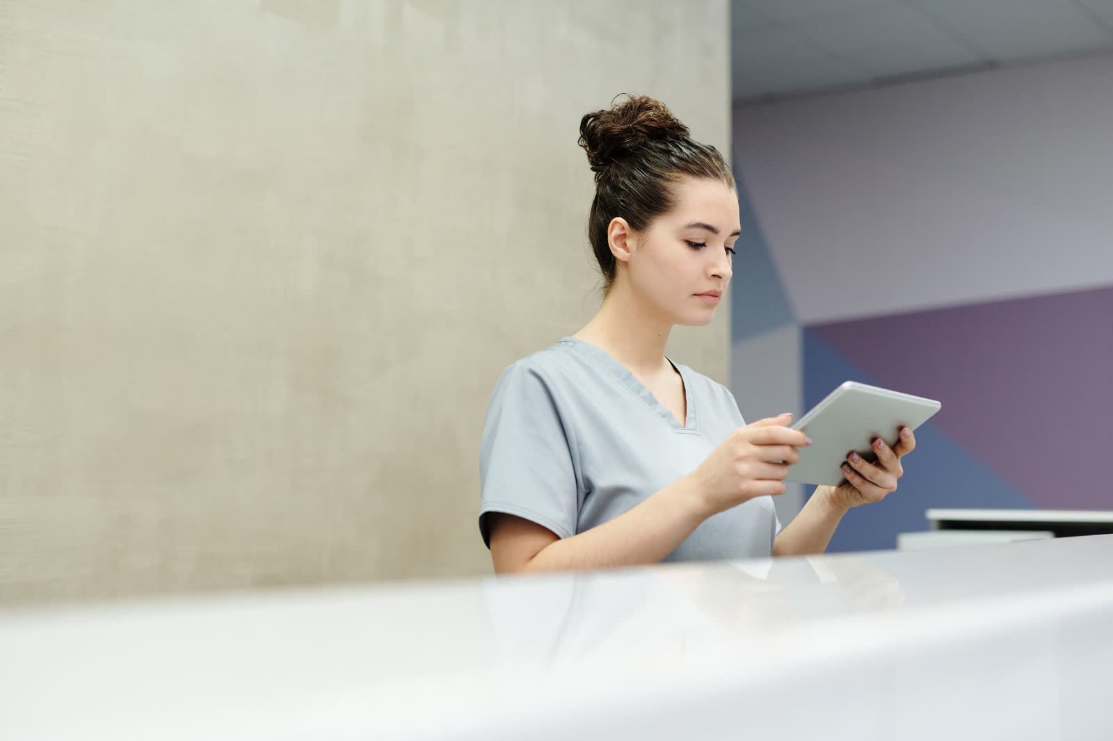 Une personne en blouse consulte une tablette au comptoir d’accueil d’une clinique